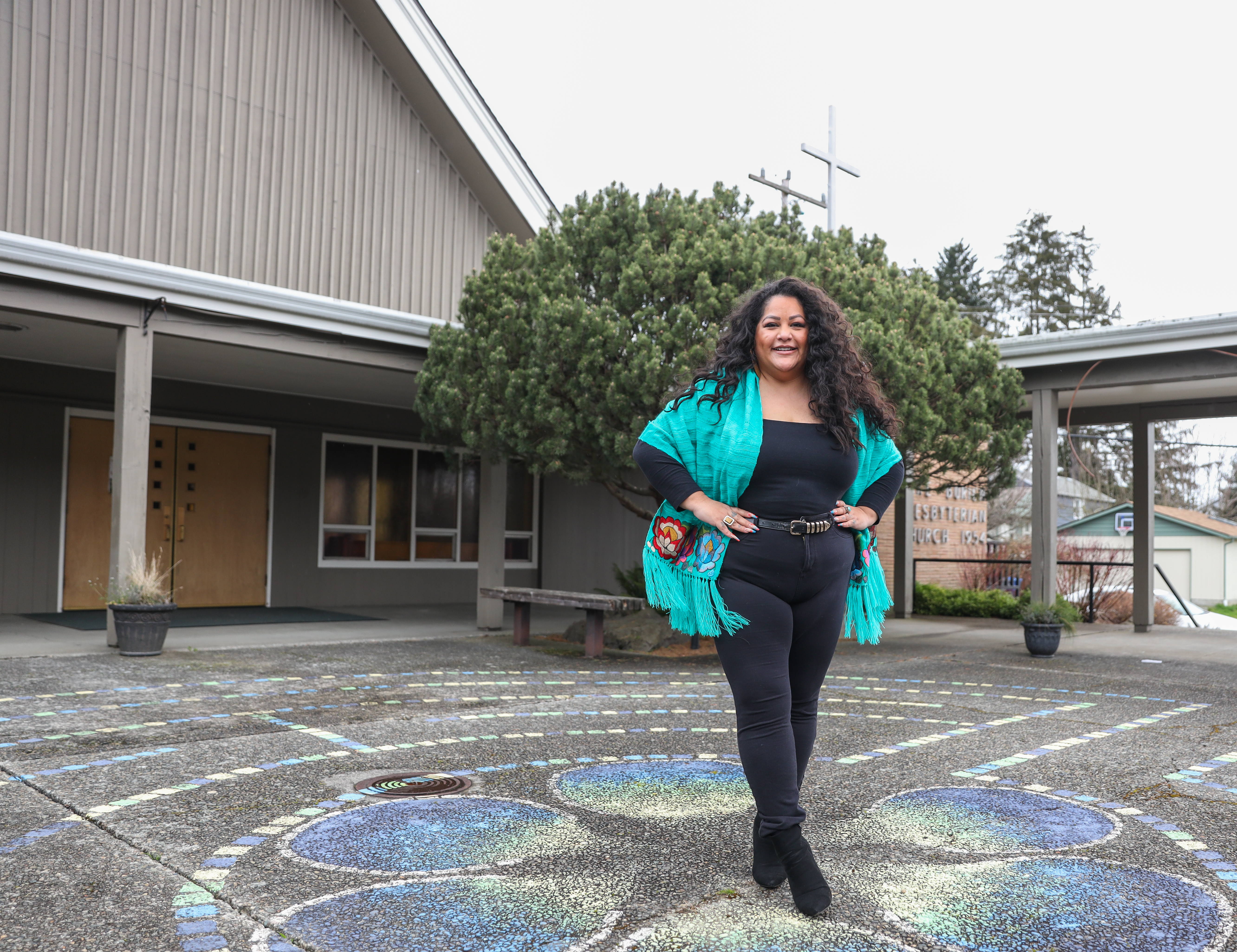 Roxana, wearing a turquoise shawl, black pants and shirt standing in front of the Lake Burien Presbyterian Church ©️ Bill & Melinda Gates Foundation/Alex Garland