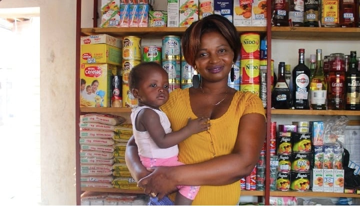 Woman holding a baby in front of food stocked shelves